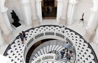 A circular staircase leads down from a round gallery with statues in its alcoves