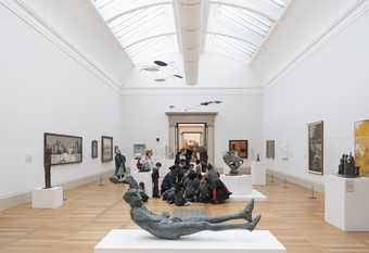 A school group in a gallery space featuring several sculptures and paintings